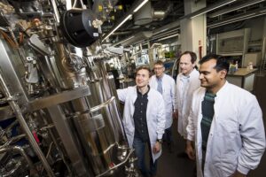 Den danske biotek-virksomhed Cysbio er klar med ny teknologi til fremstilling af svært producerbare biokemikalier med minimal miljøbelastning. Markedsperspektivet og potentialet er enormt. Med 33 millioner EU-støttekroner i ryggen kan den danske biotekvirksomhed Cysbio fremstille både billigere og mere miljørigtige biokemikalier. Virksomhedens patenterede fermenteringsteknologi rummer et enormt potentiale og markedsperspektiv for storproduktion af ellers svært producerbare kemikalier som aminosyrer og ålegræssyre til brug indenfor fødevareindustrien, landbruget og skibsfarten. Ifølge Henrik Meyer, der er CEO i Cysbio, giver EU-støtten virksomheden en gylden mulighed for at høste frugterne af mange års forskning og udvikling. – Teknologien har været under udvikling i 10 år, og vi er nået dertil, hvor de første aminosyrer og sulfaterede produkter relativt snart kommer på markedet. Vi kan nu fremstille mikroorganismer på en måde, som ingen andre kan, og med støtten fra EU kan vi speede processen op og køre den i stor målestok. Det betyder, at vi hurtigere end forventet kan udvikle nye og svært producerbare biokemikalier, hvor mikroorganismer omdanner vedvarende kulstofråvarer såsom sukker til de ønskede slutprodukter, fortæller Henrik Meyer. Aminosyrer kan forebygge sygdomme Cysbio vil bruge 15 millioner af støttekronerne på at gøre fremtidens brug af aminosyrer mere miljørigtig. Målet er en markant omlægning af verdensproduktionen af en række aminosyrer, som i dag bruges i en bred vifte af produkter inden for blandt andet fødevarer, foder, kosmetik, kosttilskud og pharma. – Med vores forskning har vi udviklet en helt ny metode, hvor vi meget billigere end tidligere kan fremstille i første omgang to vigtige aminosyrer, som grundet vores lave omkostninger kan erstatte en lang række produkter og tilmed give basis for helt nye anvendelser, som den hidtidige høje pris har umuliggjort. Dermed kan vi være med til markant at reducere verdens forbrug af kemisk fremstillede aminosyrer, siger Alex Toftgaard Nielsen, der er CSO i Cysbio. Serin er en af disse aminosyrer, som i dag kun bruges i begrænsede mængder. Nyere forskning har vist, at sygdomme så som fedtlever og andre markante livsstilsygdomme effektivt kan forebygges eller behandles gennem et dagligt indtag af serin som kosttilskud. På verdensplan vurderes det at op mod 20 procent af verdens befolkning har eller er i risiko for at udvikle fedtlever. – Den lavere produktionspris vil muliggøre en bred tilgængelighed af sådanne serin-tilskud, samtidig med at produktionen baseres på en bæredygtig produktionsmetode, siger Alex Toftgaard Nielsen. Grønnere skibsfart i udsigt Den resterende del af støtten vil Cysbio bruge til at gøre en lang række byggematerialer og malingstyper mere miljørigtige. Med fermenteringsteknologien kan virksomheden fremstille både billigere og mere bæredygtig ålegræssyre, som kan reducere mængden af biofilm i mange forskellige produkter uden at det skader miljøet. – Når vi fremstiller ålegræssyre, kan vi eksempelvis skåne havmiljøet massivt. For at reducere mængden af biofilm på skibe males der i dag med kemisk og kobberholdig maling. Det gør man for at fjerne biofilm, der får skibene til at sejle langsommere, men metoden er både dyr og meget skadelig for miljøet. Med ålegræssyre kan vi udskifte de skadelige komponenter med mere miljørigtig kemi, siger Alex Toftgaard Nielsen. Ifølge Cysbio bruges der globalt set over en milliard liter maling til skibe årligt, mens de vurderer markedsværdien til at være på omkring 2,5 milliarder USD med en årlig vækst på fem procent. Desuden er der et meget stort behov for miljørigtige alternative ingredienser med antifouling egenskaber, så potentialet for en miljømæssig og økonomisk gevinst er meget stort, lyder vurderingen fra Alex Toftgaard Nielsen. Cysbio anvender avanceret teknologi til at skabe billige og bæredygtige biokemikalier ved at modificere mikroorganismer og gøre dem i stand til at omdanne simple sukkerater til biokemiske produkter. Cysbio er et spin out fra Novo Nordisk Foundation Center for Biosustainability ved DTU (Danmarks Tekniske Universitet). Se mere på www.cysbio.dk